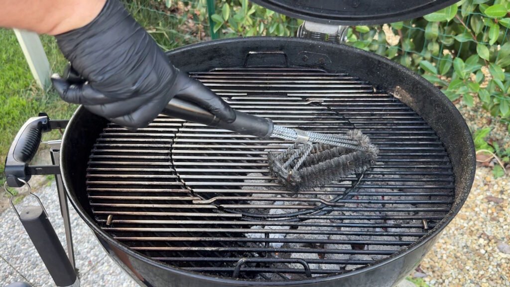 Spazzola in acciaio che pulisce energicamente le griglie roventi di un barbecue per rimuovere i residui di cibo.