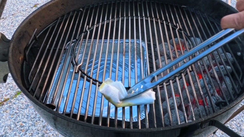 Pinza da barbecue che tiene un tampone di carta imbevuto d'olio per lubrificare le grate calde prima della cottura.