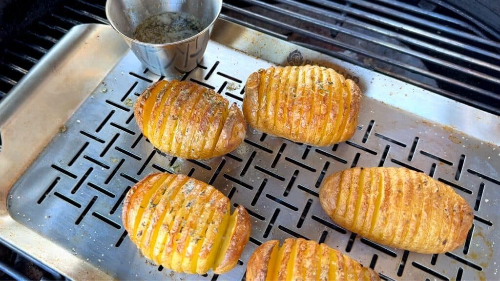 Patate Hasselback in cottura su vassoio di acciaio sulla griglia del barbecue