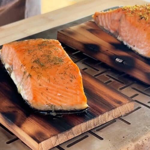Risultato finale del salmone su placca di cedro appena tolto dal barbecue: due filetti succosi e affumicati con variante al lime e al burro all'aneto pronti per essere serviti.