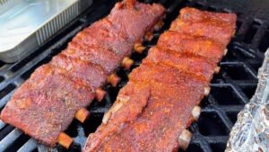 Primo piano del bark sulle costine di maiale in cottura, con la carne che inizia a ritirarsi esponendo le ossa