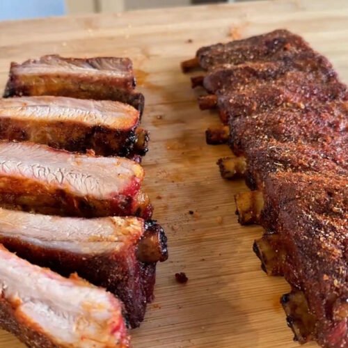 Costine al barbecue a gas tagliate sul tagliere in legno, con il bark speziato croccante e la carne interna succosa