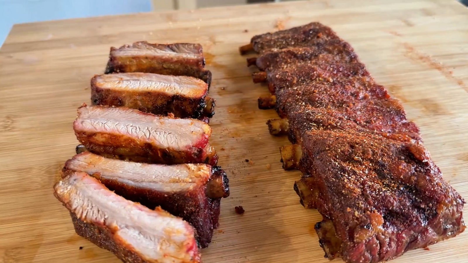 Costine al barbecue a gas tagliate sul tagliere in legno, con il bark speziato croccante e la carne interna succosa