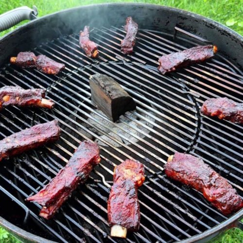 Party ribs glassate disposte ad anello sulla griglia del kettle Weber, intorno al Vortex con un chunk di legno al centro